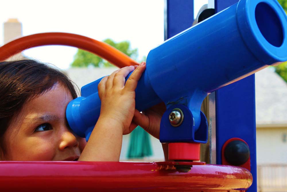 child looking through telescope at playground